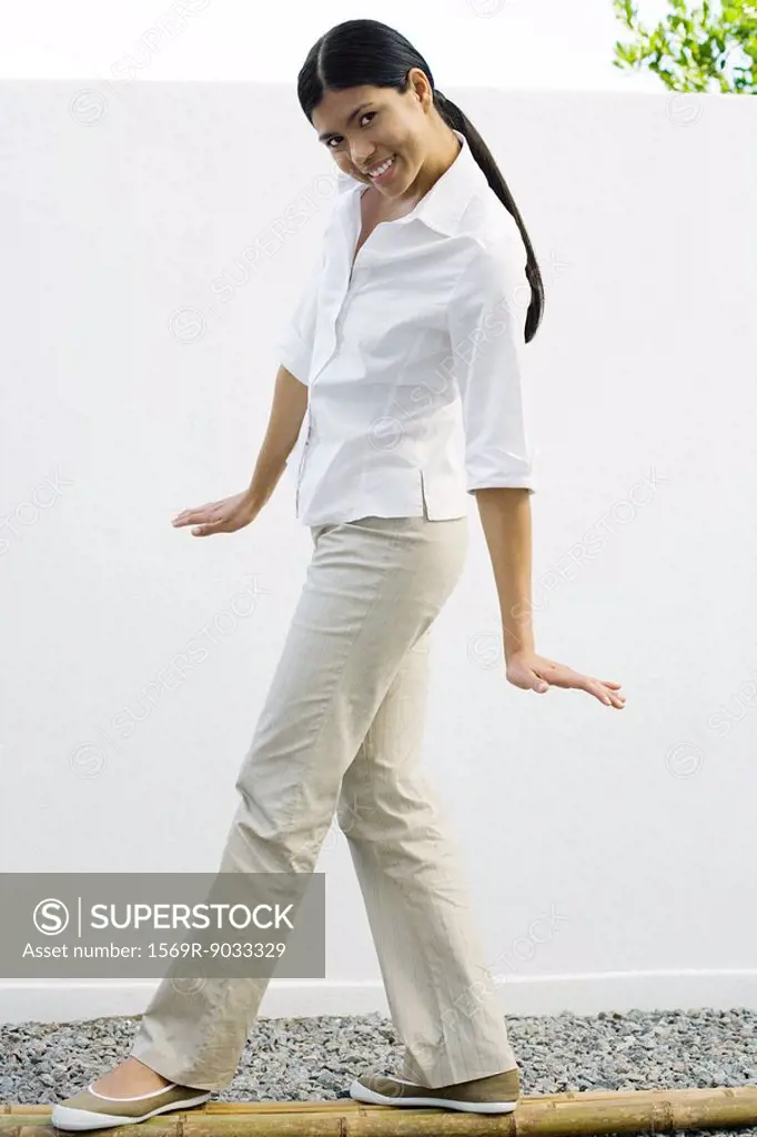 Woman standing on bamboo poles, smiling at camera, full length
