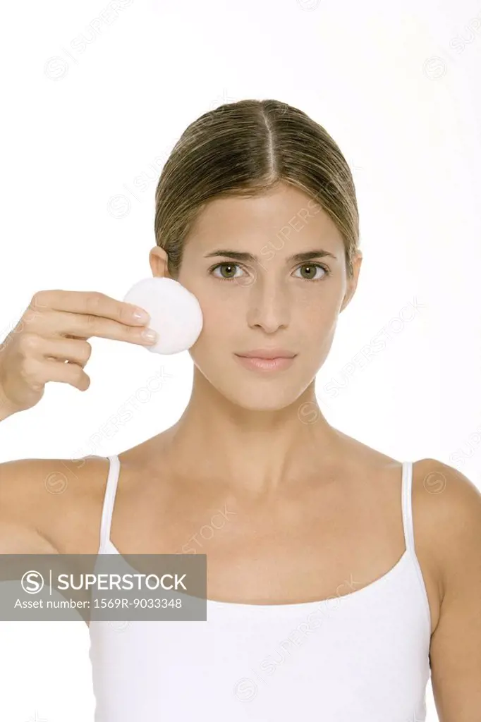 Woman holding up cotton pad to face, looking at camera
