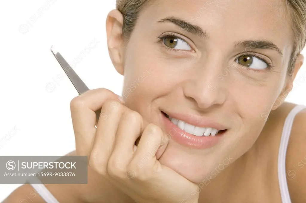 Woman holding tweezers, smiling and looking away