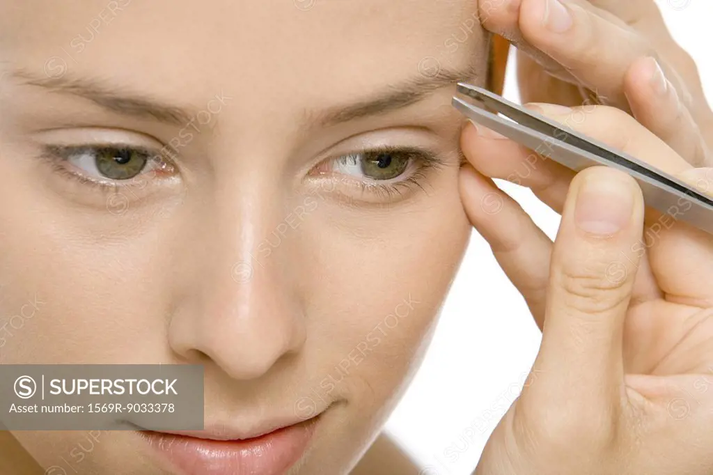 Woman using tweezers to pluck eyebrows, close-up