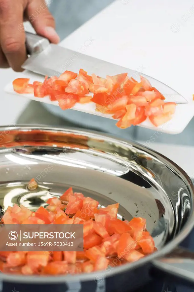 Man scraping diced tomatoes into saucepan with knife, cropped view