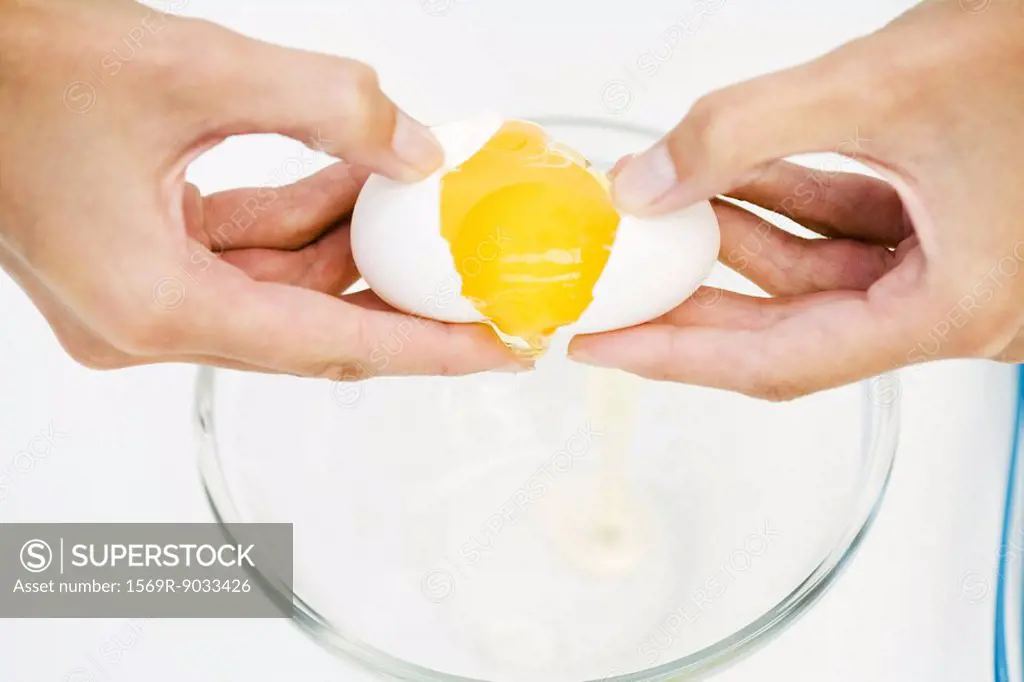 Woman cracking egg into mixing bowl, cropped view of hands, high angle view