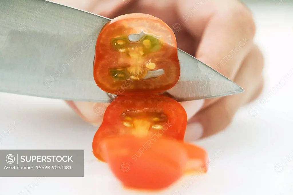 Woman slicing tomato with knife, cropped view of hand