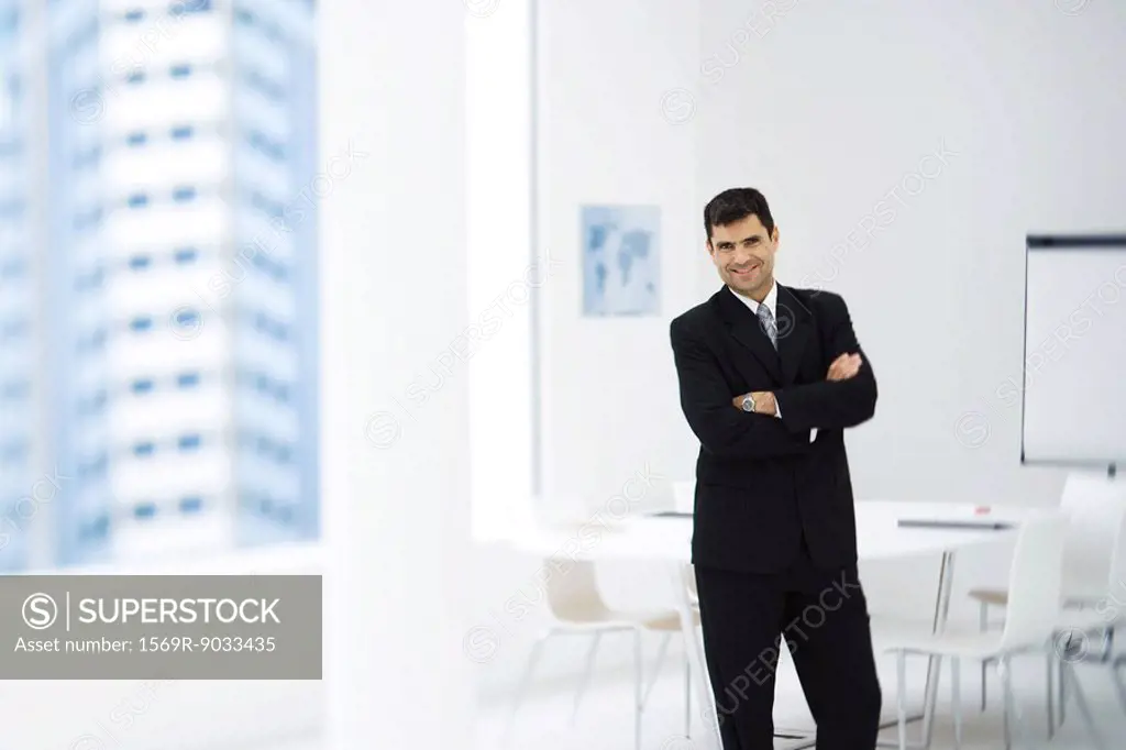 Businessman standing in meeting room with arms crossed, smiling at camera