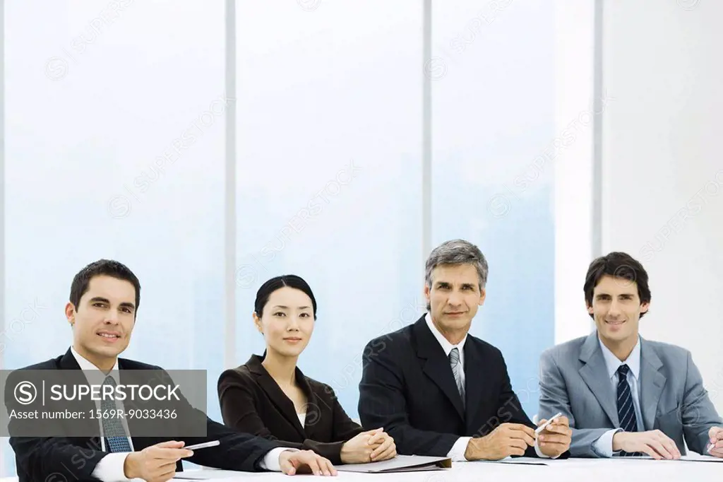 Business associates sitting at meeting table, smiling at camera