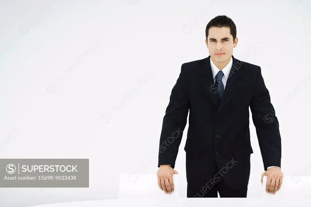 Businessman leaning on backs of chairs, looking at camera