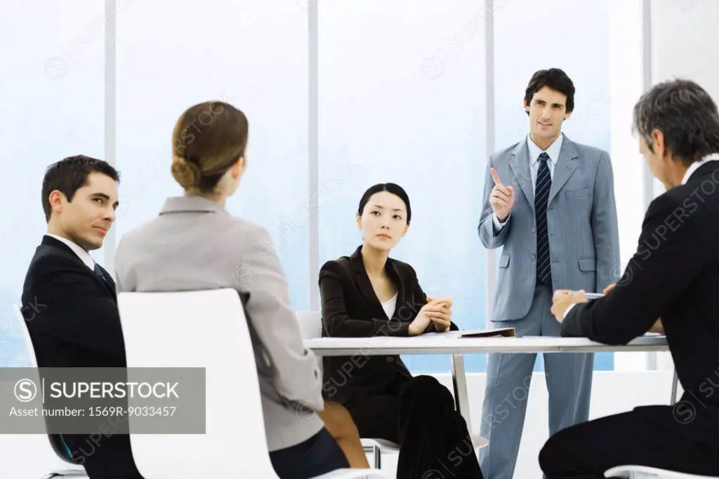 Business associates having meeting, one standing, pointing