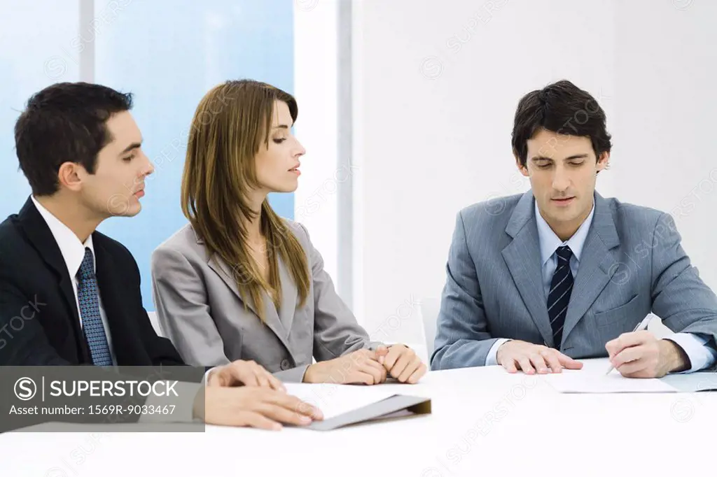 Business associates in meeting, man signing document while others watch