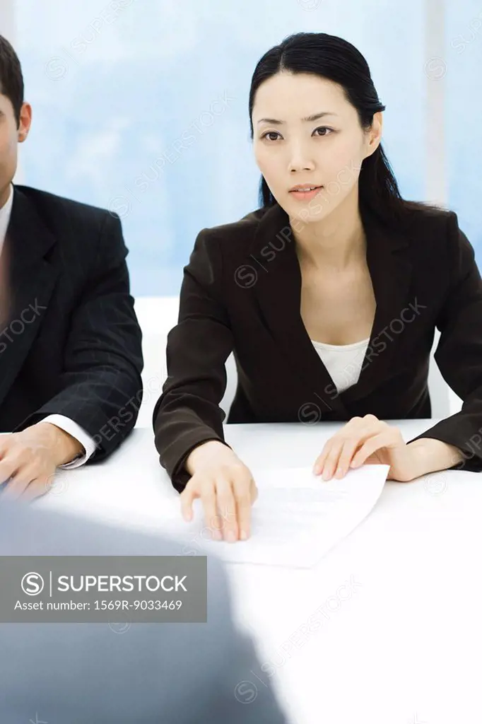 Business associates in meeting, businesswoman holding out document, looking across table