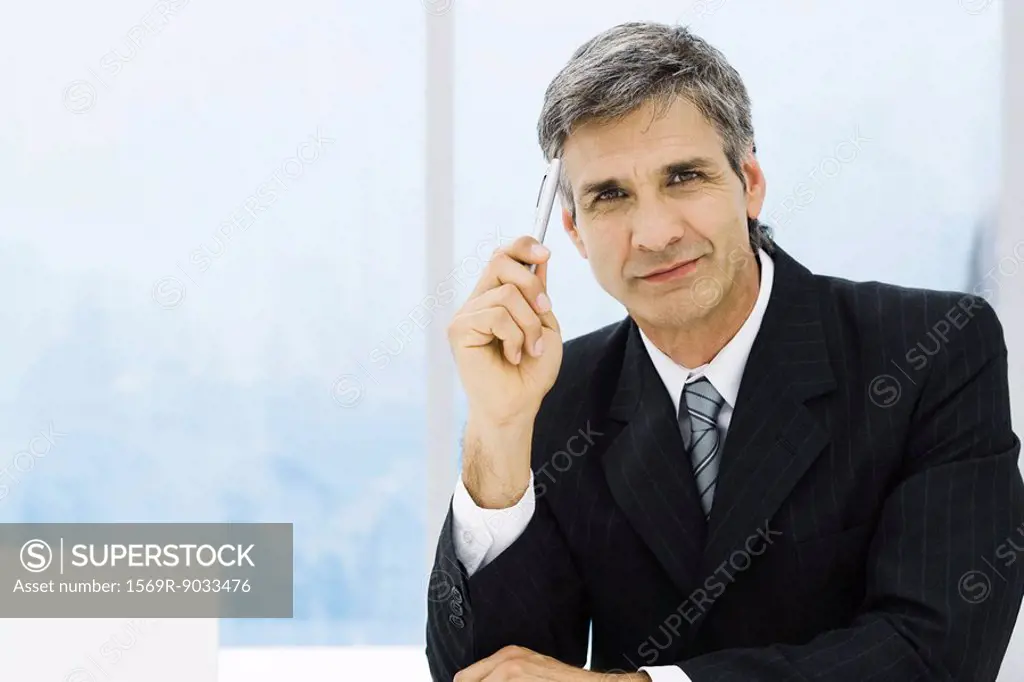 Businessman holding pen up to head, portrait