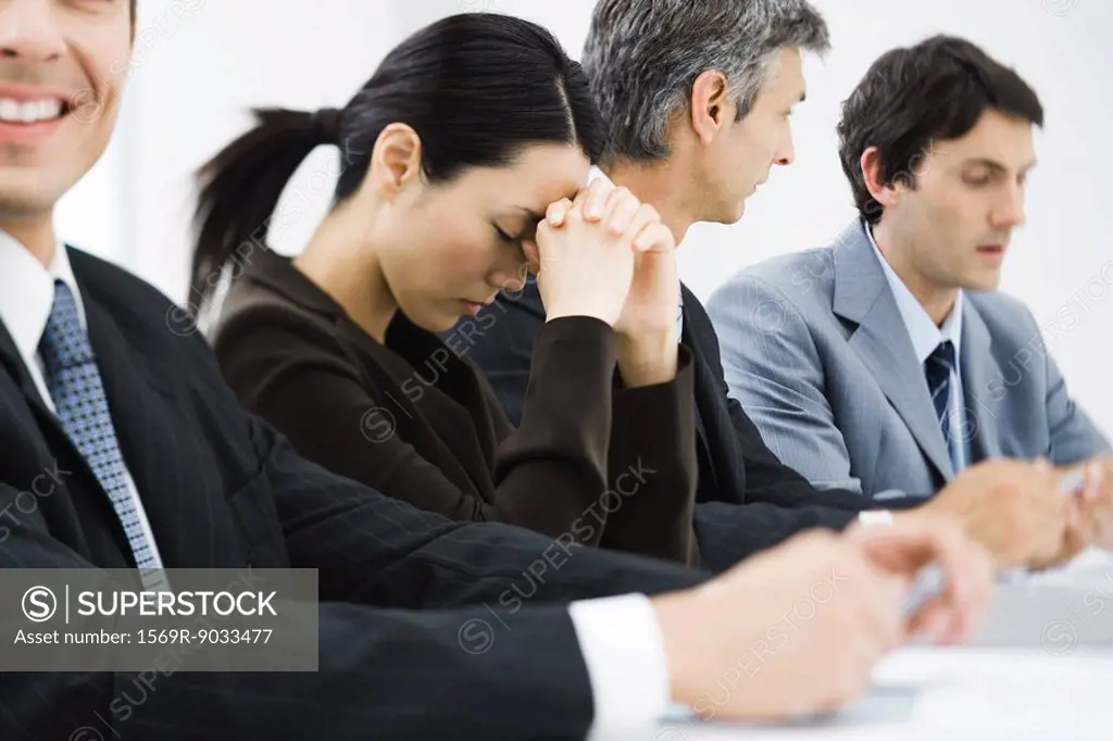 Executives in business meeting, woman closing eyes and leaning head against hands