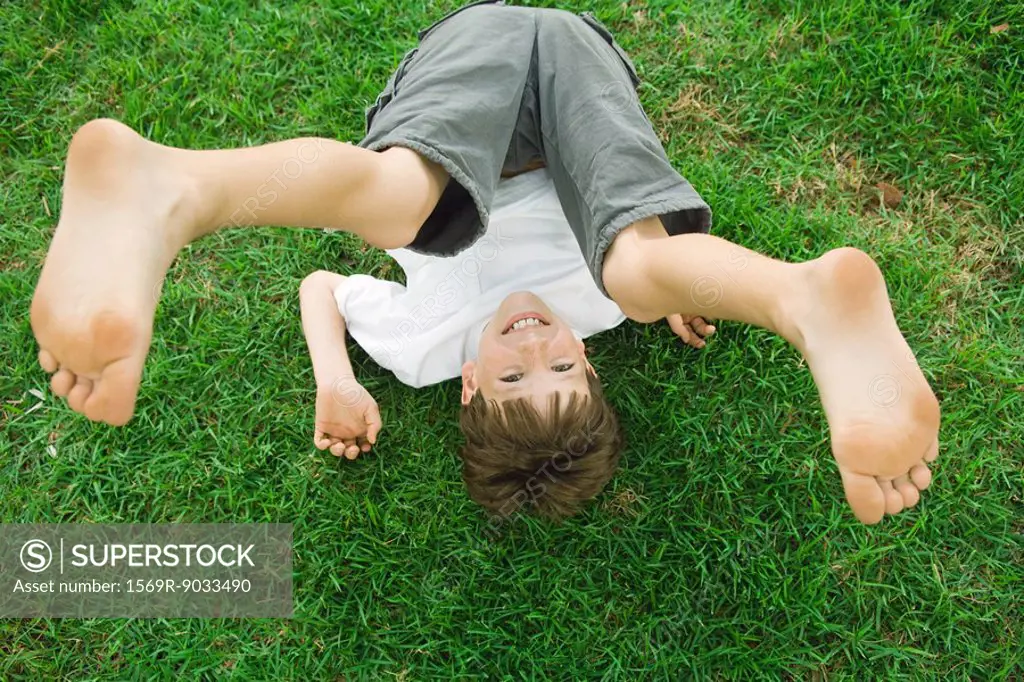 Boy lying on the ground with legs in the air, smiling at camera, high angle view