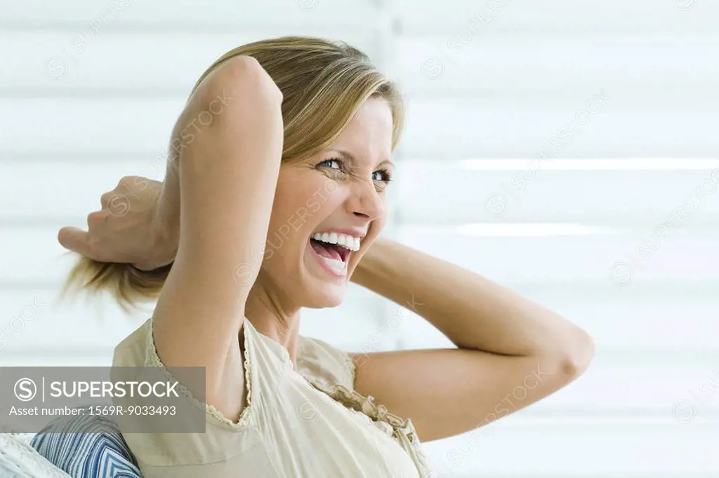 Woman pulling hair back with hands, laughing, side view