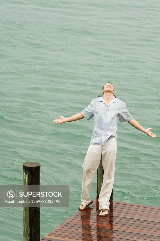 Man leaning back on pier in the rain, arms out, eyes closed, high angle view
