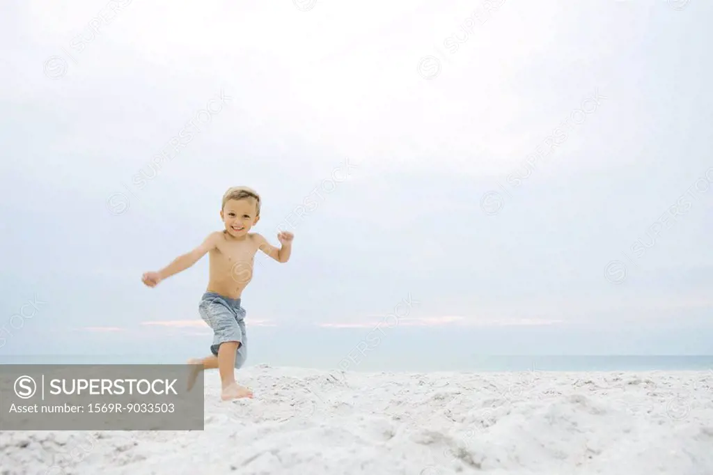 Little boy running at the beach, smiling at camera