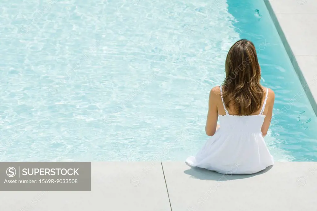 Woman sitting on edge of swimming pool, rear view, high angle