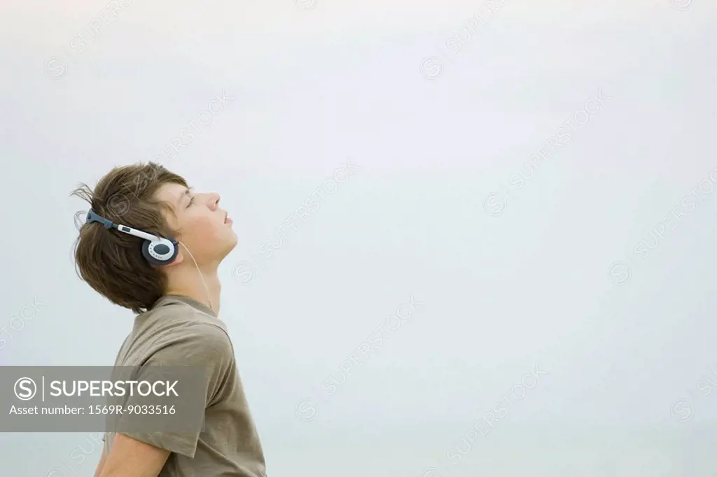 Teenage boy listening to headphones, looking up, side view
