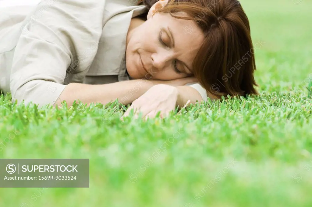 Woman lying on grass with head resting on arms, eyes closed