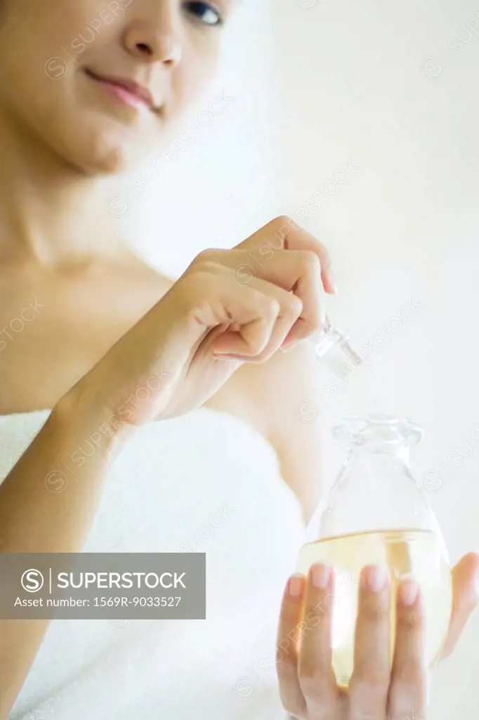 Woman wrapped in towel opening perfume bottle, smiling at camera, cropped view