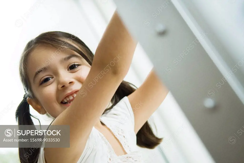 Little girl with pigtails smiling at camera, arms raised, portrait