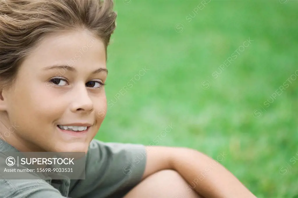 Boy sitting outdoors, smiling at camera, close-up