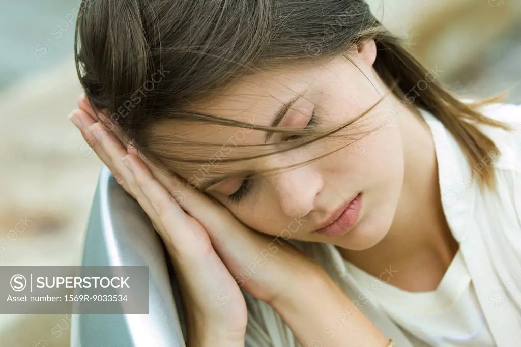 Teenage girl resting head on clasped hands, eyes closed, high angle view