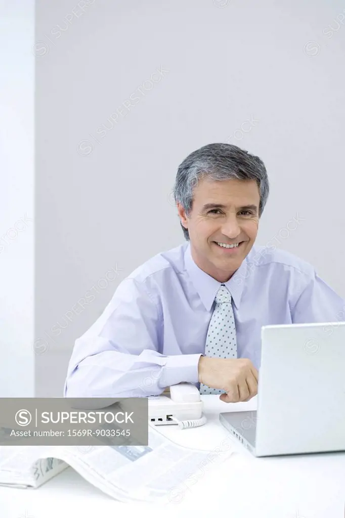 Businessman sitting at desk, smiling at camera