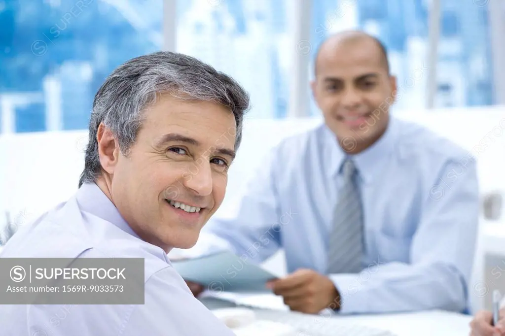 Two businessmen in office, smiling at camera