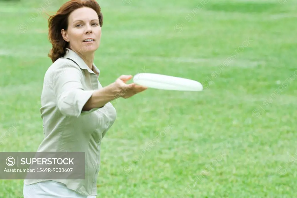 Woman throwing plastic disc, smiling at camera