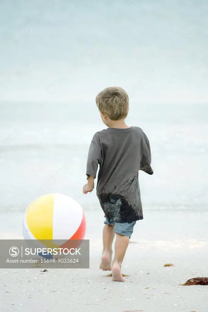 Little boy chasing beach ball at the beach, rear view