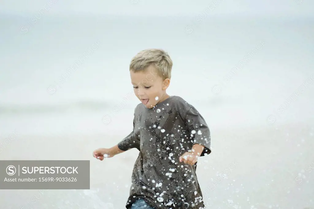 Little boy splashing water at the beach, looking down