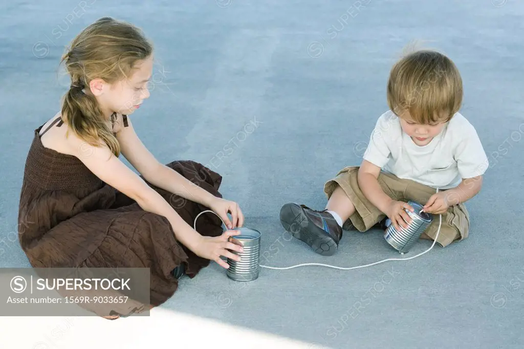 Brother and sister sitting on the ground, playing with tin can phone