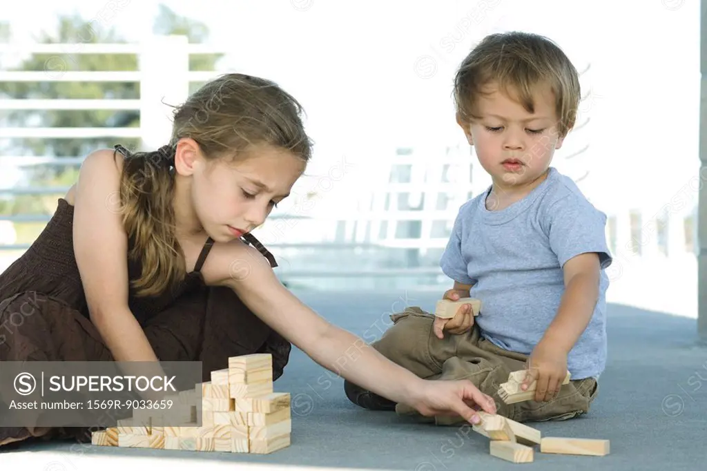 Brother and sister sitting on the ground, playing with building blocks together