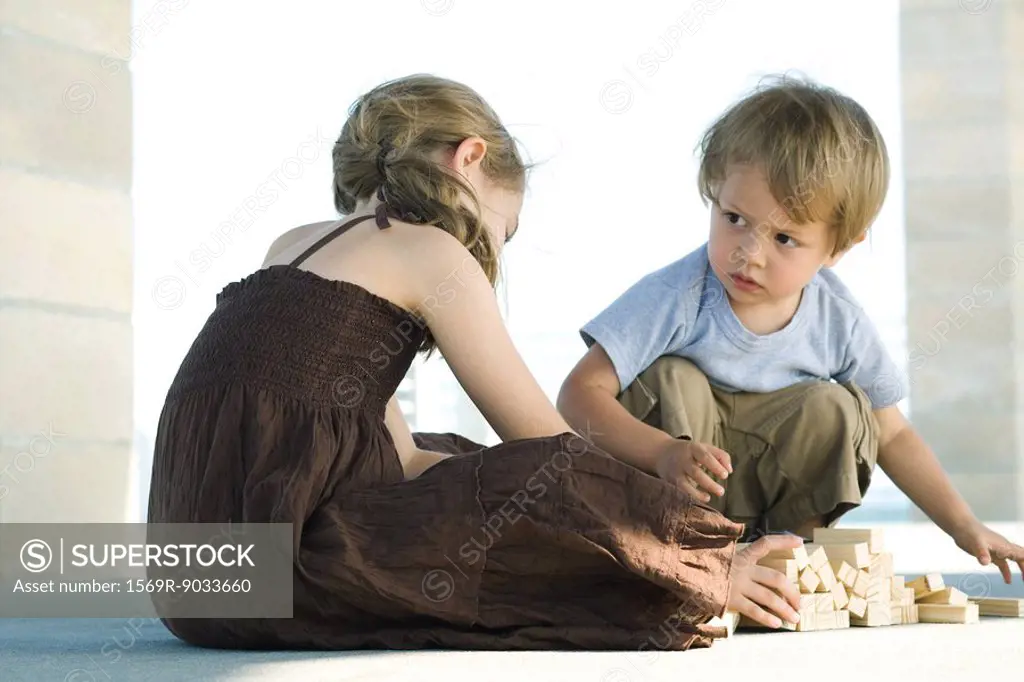 Boy and girl sitting on floor, playing with building blocks