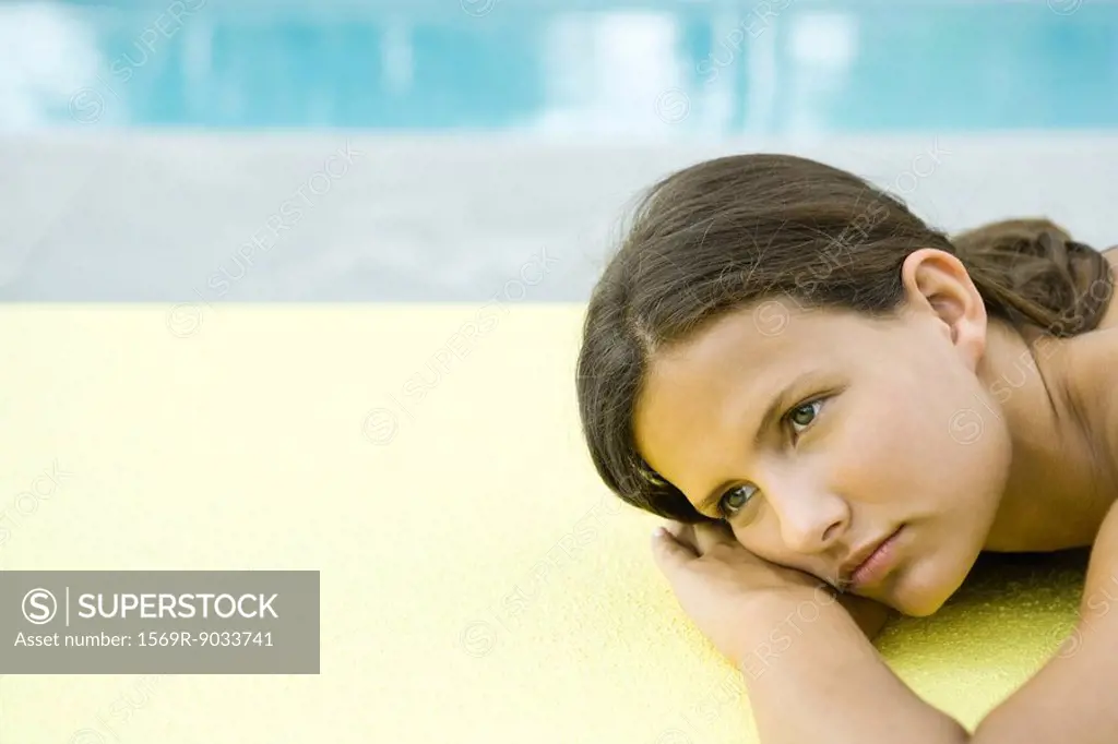 Teenage girl lying on stomach, head resting on arms, looking away
