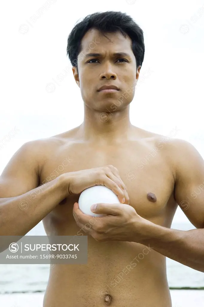 Man holding ball in cupped hands, topless, looking away