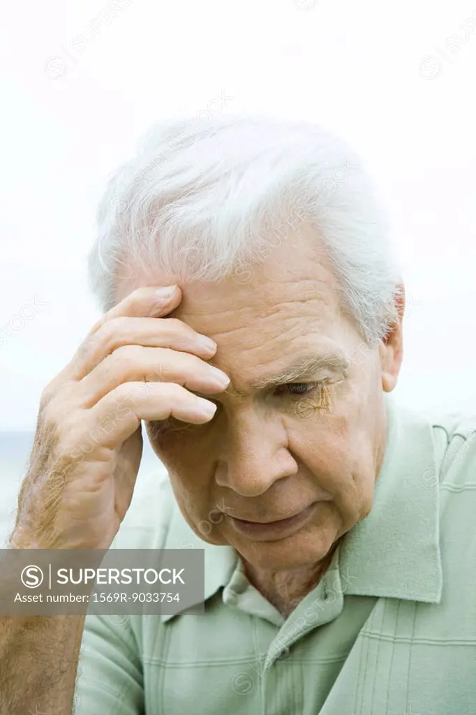 Senior man holding head, looking down, close-up