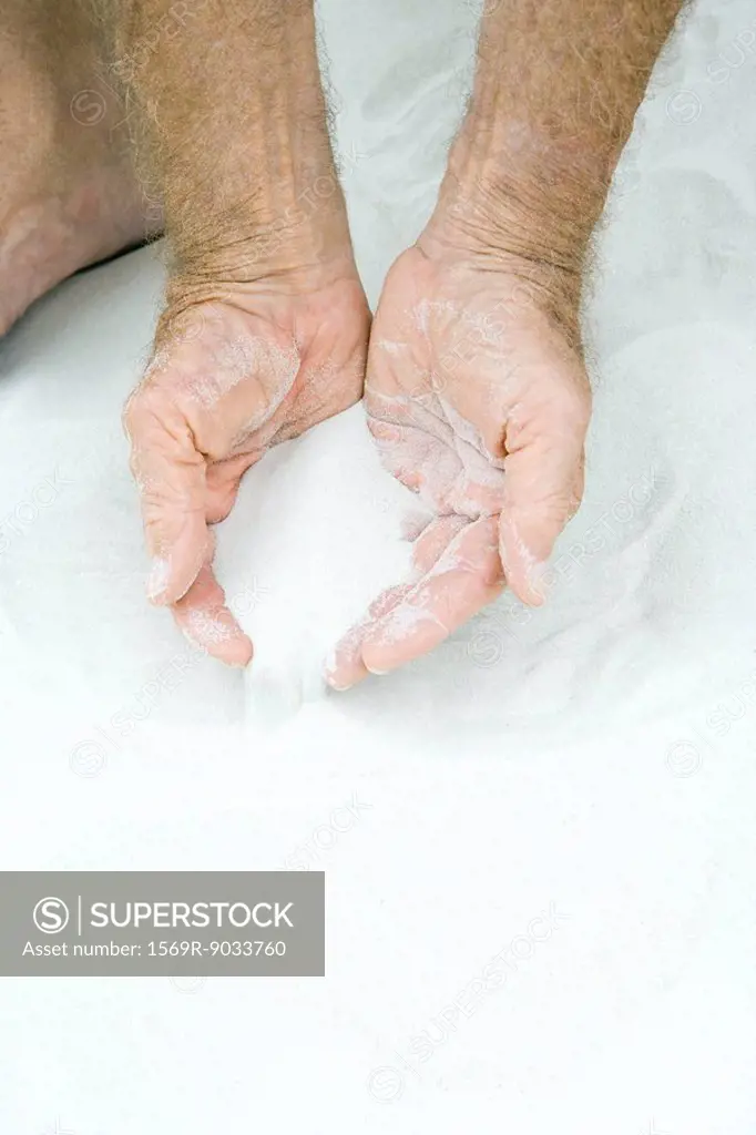 Man scooping sand in both hands, cropped view of hands