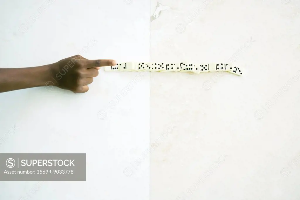 Child knocking over line of dominoes, cropped view of hand