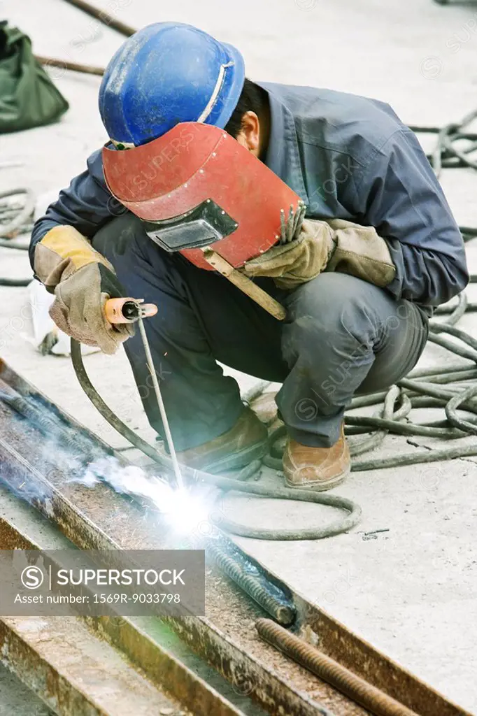 Worker welding metal rod at construction site, close-up