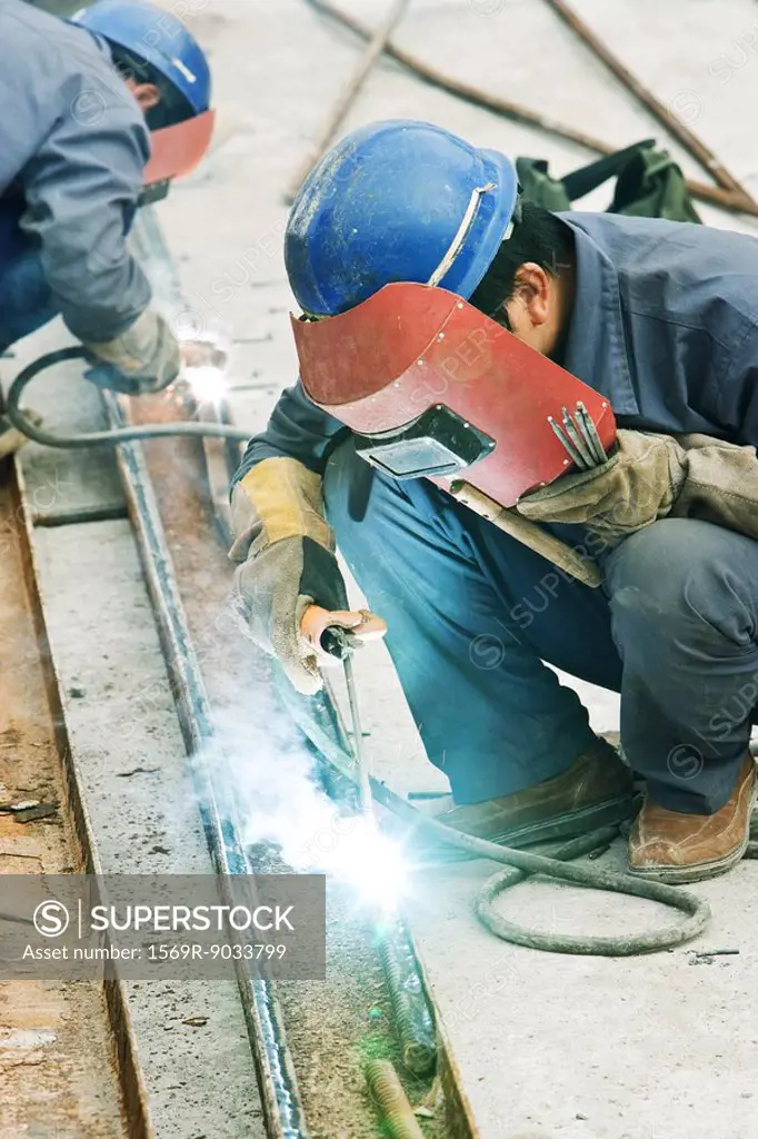 Worker using welding torch at construction site, side view