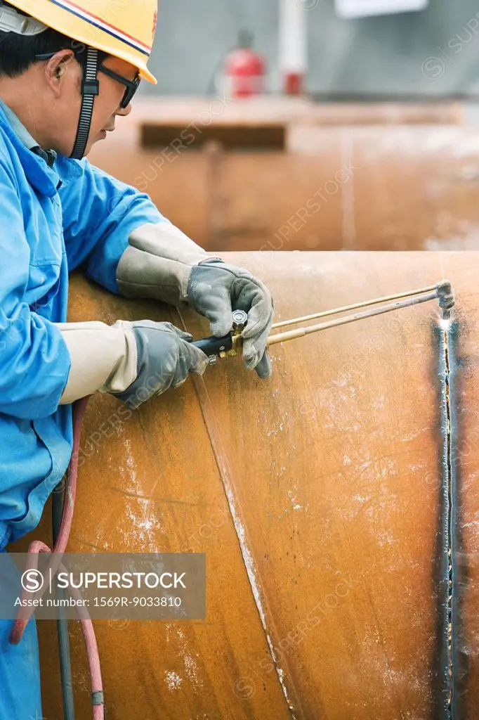Man cutting metal with welding torch, side view, cropped