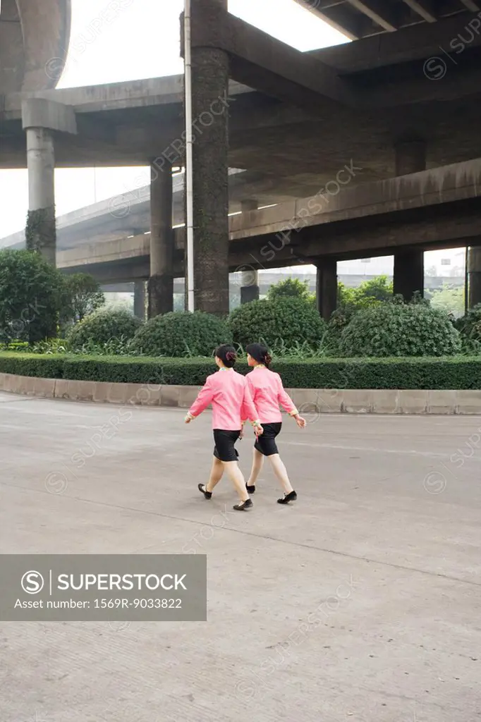China, Guangzhou, two woman wearing matching uniforms walking under bridge, rear view