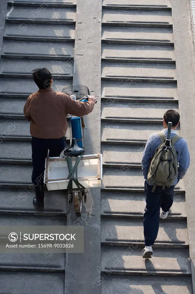 Pedestrians walking up steps, one pushing bicycle, viewed from directly above