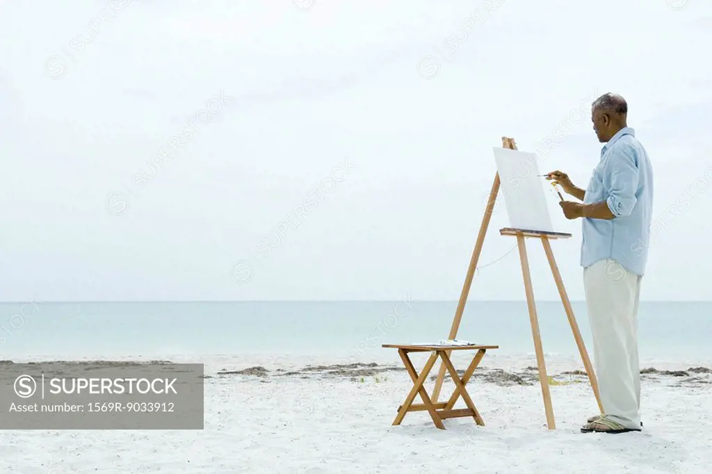 Senior man painting on canvas at the beach, side view