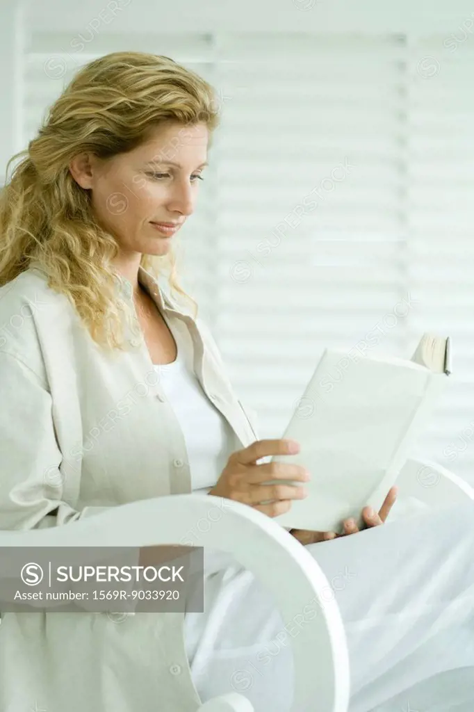 Woman sitting in rocking chair, reading book, smiling
