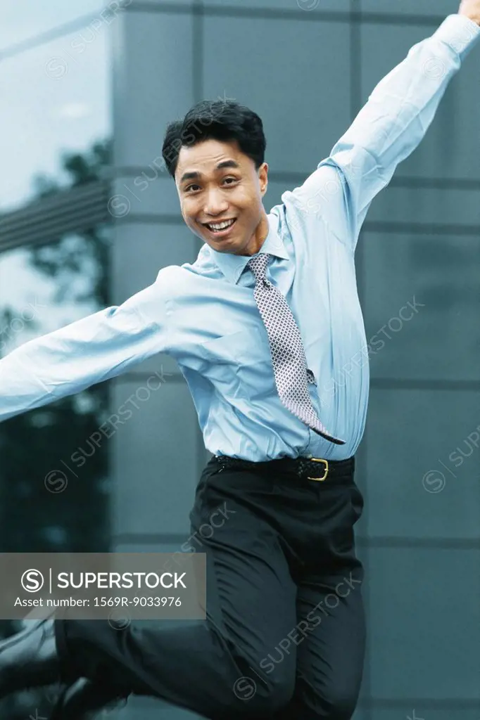 Businessman jumping in the air, arms out, smiling at camera