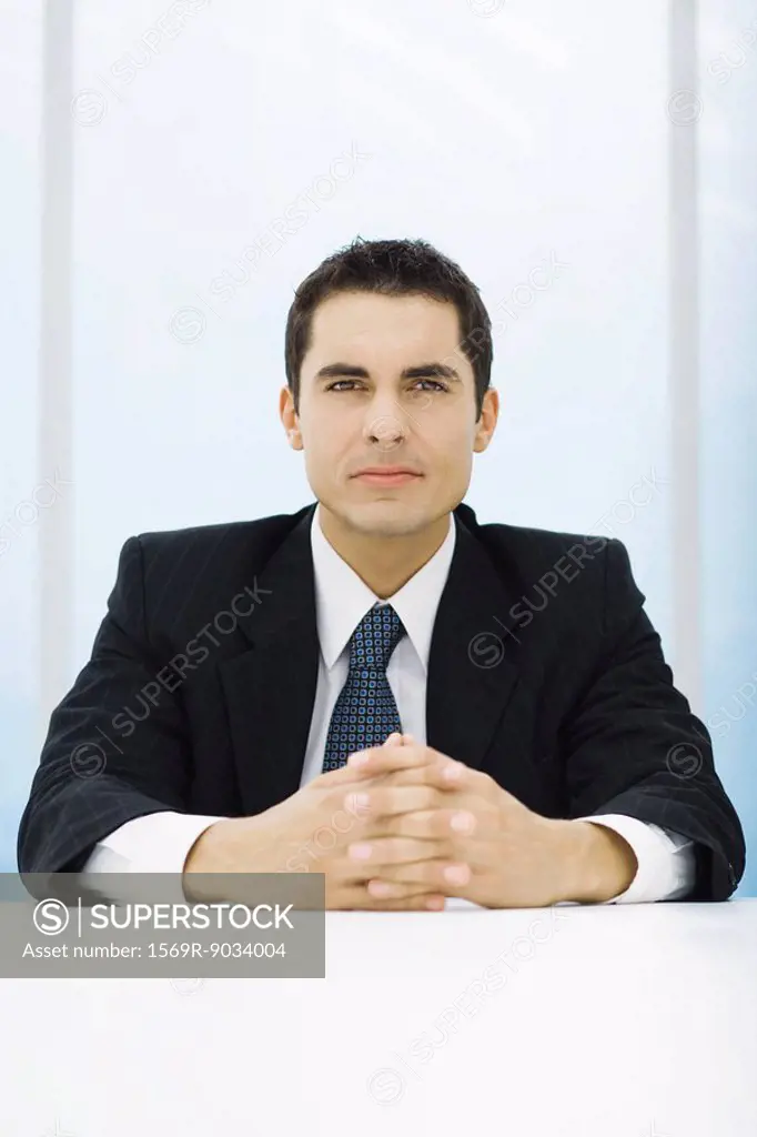Businessman sitting at table with clasped hands, looking at camera