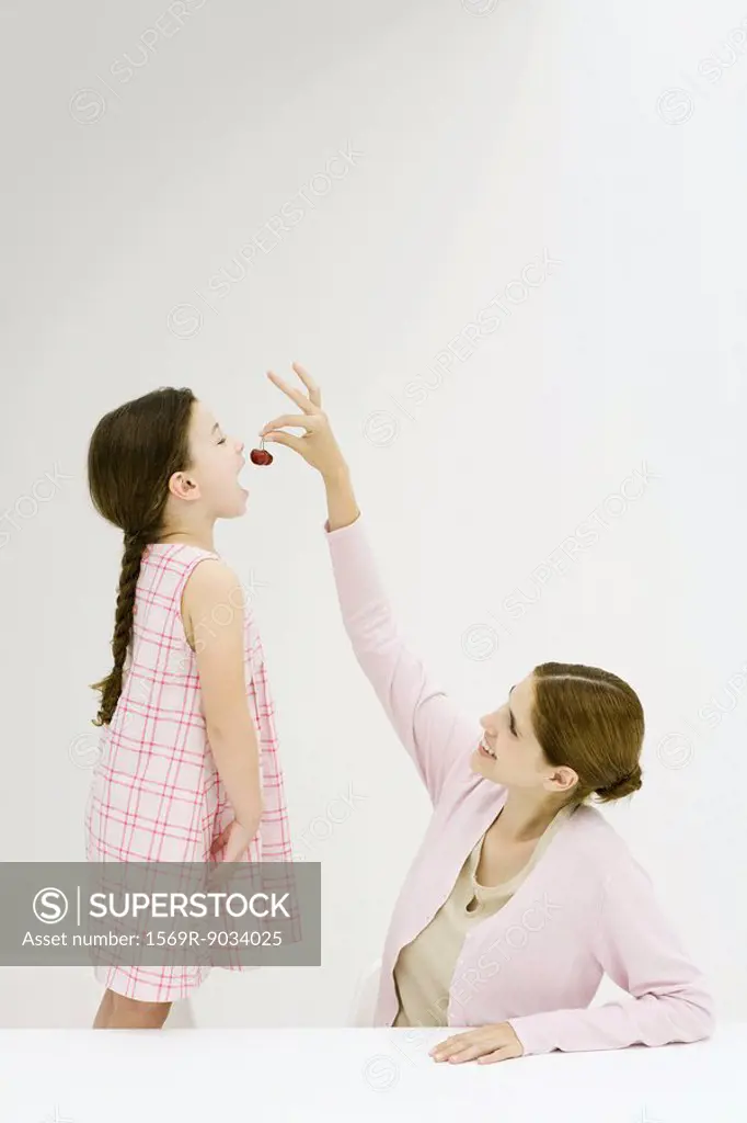 Woman feeding little girl cherries