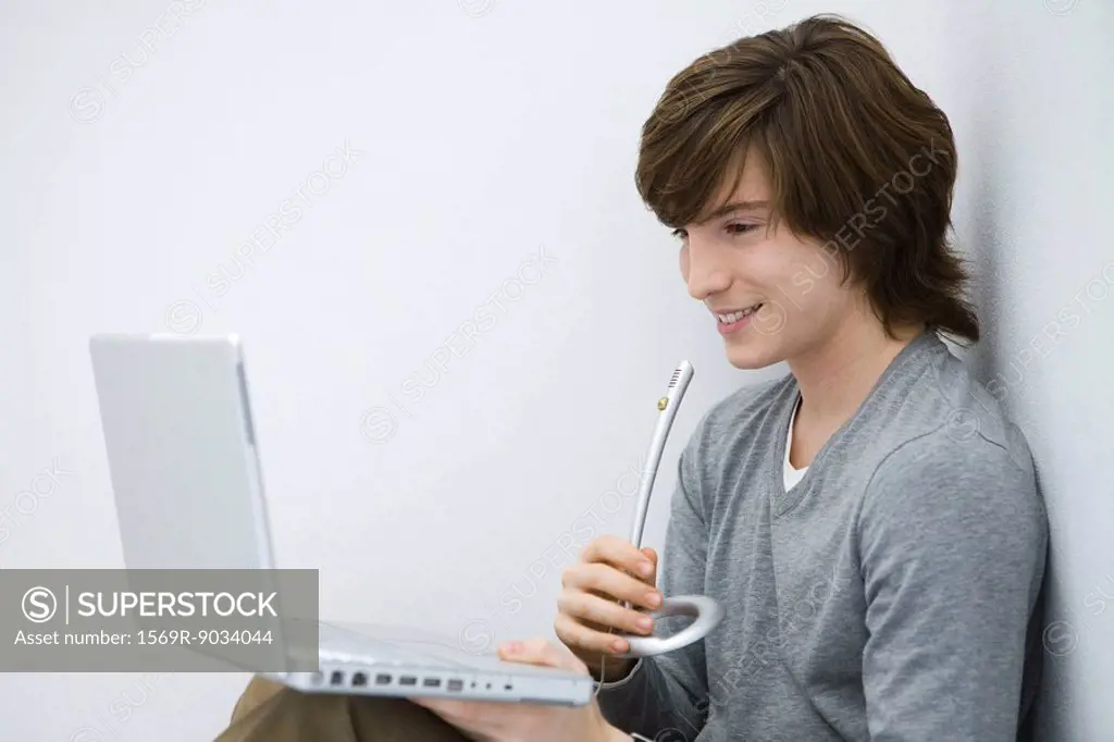 Young man looking at laptop computer, speaking into microphone, side view